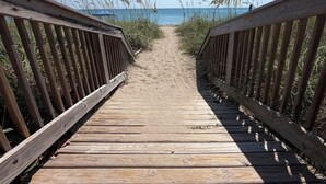 Ein hölzerner Steg führt zu einem Strand unter blauem Himmel.