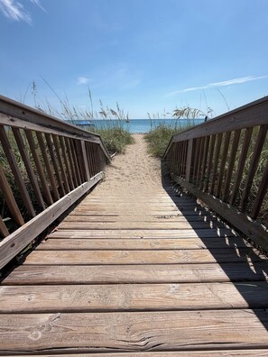 Ein hölzerner Steg führt zu einem Strand unter blauem Himmel.