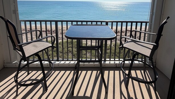 Ein Balkon mit Tisch und zwei Stühlen mit Blick auf einen Strand und das Meer.