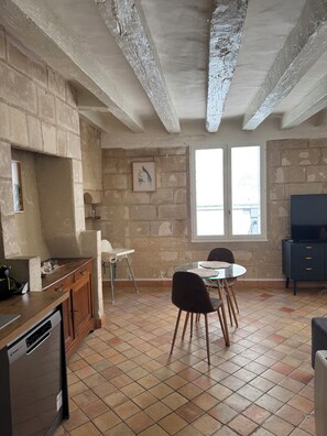 Een keuken met een vaatwasser, een eettafel met stoelen, een tv-meubel en een raam met uitzicht.