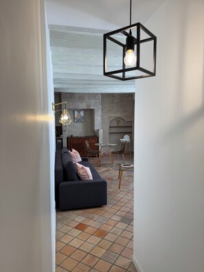 Een moderne woonkamer met een bank, een eettafel en stoelen. Er is een open haard en een hangende lamp.