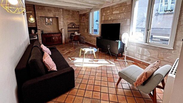 Ein Wohnzimmer mit einer Couch, einem Fernseher, einem Kamin und Blick auf die Straße durch große Fenster.