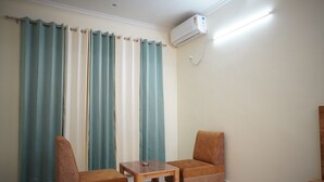 Una habitación con dos sillas marrones, una mesa de madera pequeña, cortinas color turquesa y un aire acondicionado instalado en la pared.