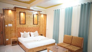 Un dormitorio con cabecera de madera, cama con ropa de cama blanca, mesita de noche de madera, una mesa de madera y un sofá.