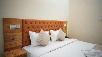 Uma cama bem arrumada com cabeceira de madeira, mesa de cabeceira com gaveta e tomada na parede.