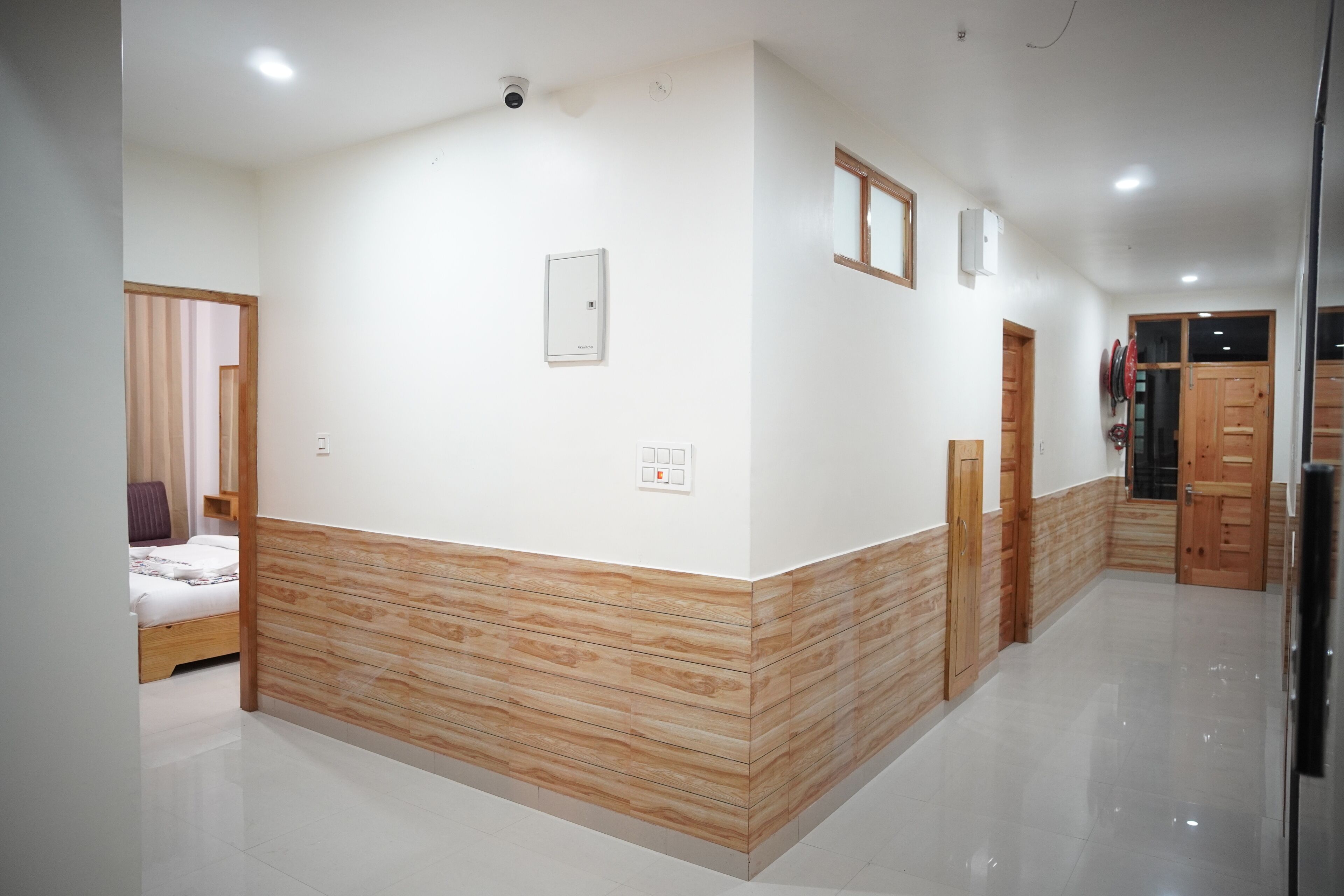 A hotel corridor with a wooden accent wall, a bed in the adjacent room, and a door leading to another room.