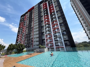 Un edificio moderno de gran altura con varias terrazas, piscina y cielo despejado.