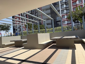 Un espace extérieur moderne doté d’une structure métallique aux lignes géométriques, d’un sol carrelé et, au fond, d’un bâtiment agrémenté de balcons.