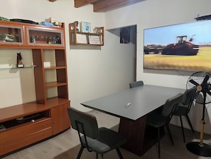 Una sala conferenze con un grande tavolo, sedie, uno schermo per proiettore, una ventola e un mobile in legno con ripiani.