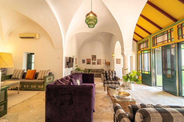 A spacious living area with a high arched ceiling, a chandelier, and a large window with a view. - Palm Paradise | 3BR Villa · Pool · La Soukra (La Soukra)