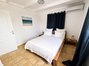 Ein Schlafzimmer mit einem Bett, einem Nachttisch, einer Wand-Klimaanlage und einem Bild mit einer Strandansicht.
