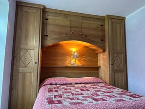 Ett sovrum med en sänggavel i trä, en säng med ett mönstrat överkast och en lampa på sänggaveln.