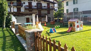 A two-story building with balconies, a play area with slides and play structures, and a fenced garden.