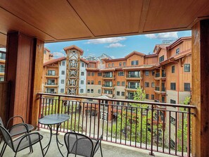 Un balcon avec une table et des chaises, donnant sur un immeuble doté de nombreux balcons et avec une chaîne de montagnes en arrière-plan.