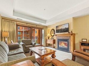 Una sala de estar con chimenea, televisor y vistas a un edificio a través de amplios ventanales.