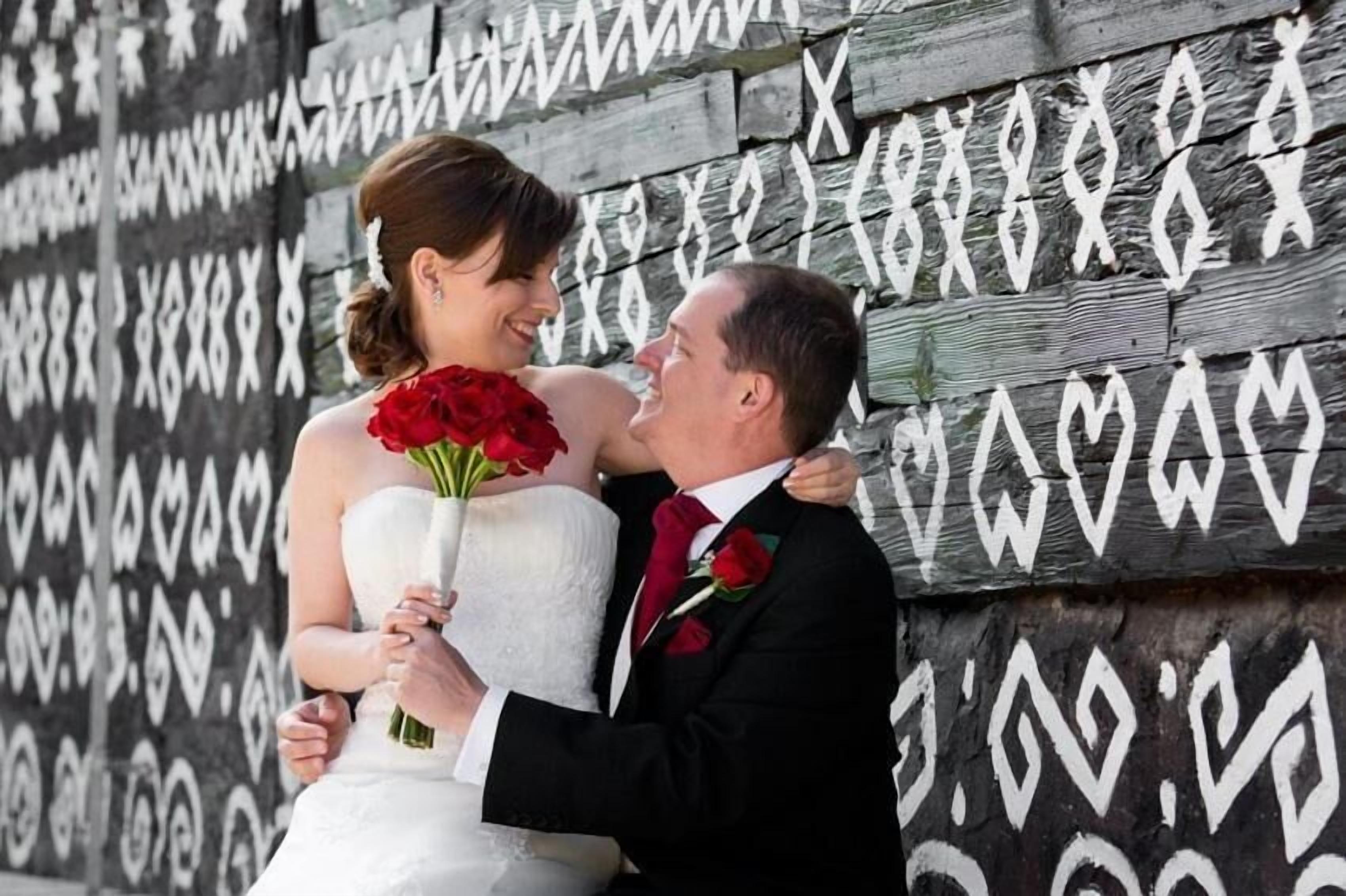 A couple embracing in front of a wall with heart patterns.