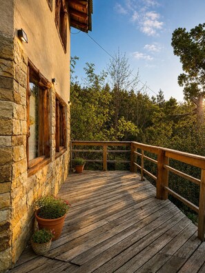 A wooden deck with stone walls, potted plants, and a view of trees. - Casa Aukan - Lake View-8 guests (San Carlos de Bariloche)