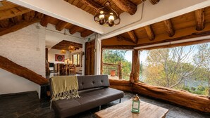 Ein gemütliches Loft-Zimmer mit einer dunkelbraunen Ledersofa, einem Holztisch und einem großen Fenster mit Blick auf Bäume.