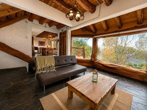 A cozy loft-style room with a dark leather sofa, a wooden coffee table, and a large window offering a view of trees. - Casa Aukan - Lake View-8 guests (San Carlos de Bariloche)