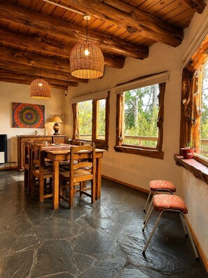 A rustic interior with a wooden dining table, chairs, a woven pendant light, and large windows with a view of greenery. - Casa Aukan - Lake View-8 guests (San Carlos de Bariloche)