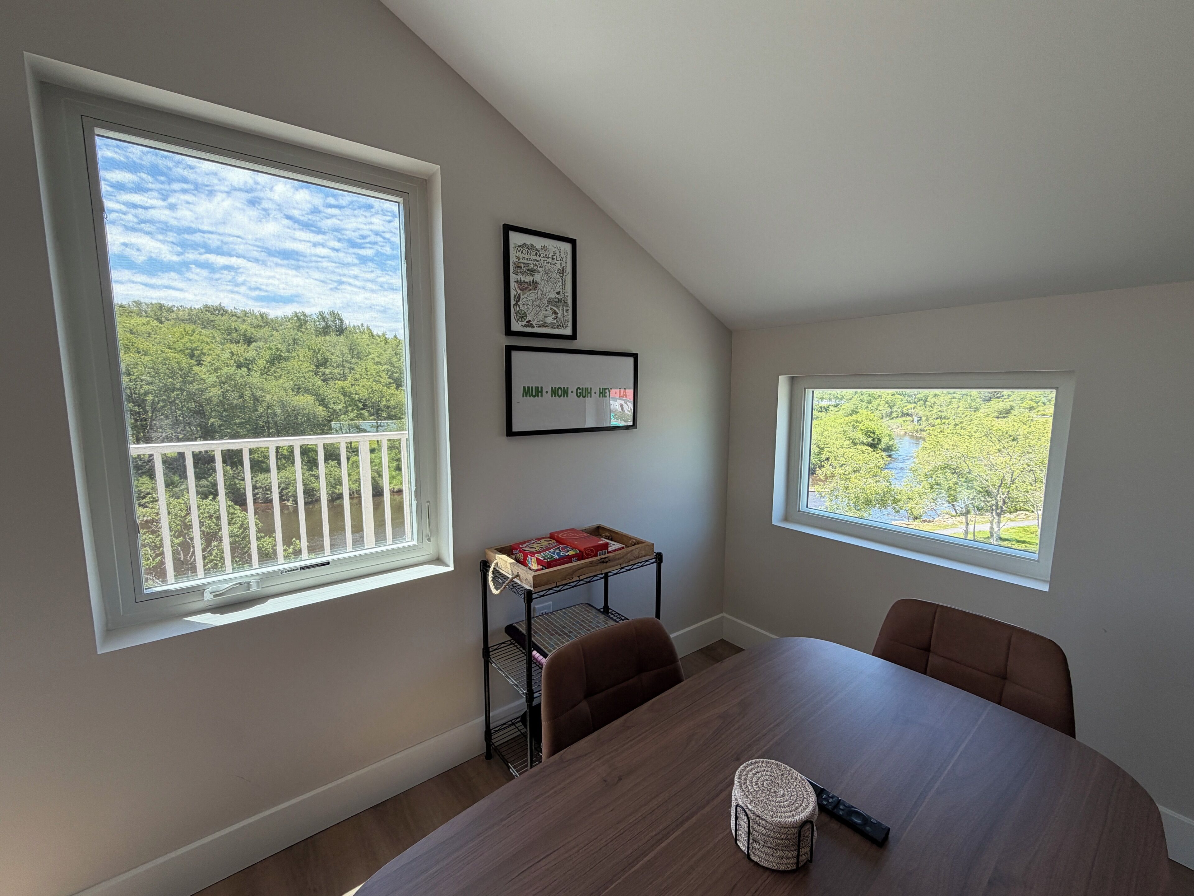 A dining area with a table, chairs, a small shelf with books, and two framed pictures on the wall.