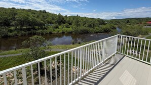 Una terraza con baranda blanca que da a un río, rodeada de abundante vegetación y árboles.