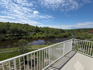 Una terraza con baranda blanca que da a un río, rodeada de abundante vegetación y árboles.