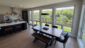 Una cocina moderna con una isla central, ventanas amplias con vistas a zonas verdes y un comedor con bancos.