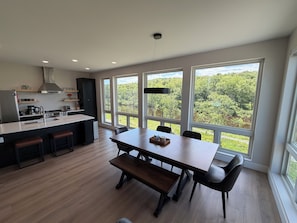 Una cocina moderna con una isla central, ventanas amplias con vistas a zonas verdes y un comedor con bancos.
