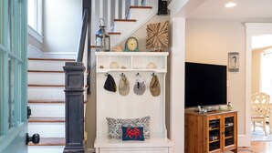 Un escalier avec un mur blanc et une rampe en bois, un banc blanc agrémenté d’objets décoratifs, un téléviseur à écran plat et un meuble en bois contenant des livres.