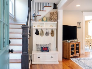Eine Treppe mit weißer Wand und einer Holzhandläufung, eine weiße Bank mit Dekorationselementen, ein Flachbildfernseher und ein Holzschrank mit Büchern.