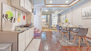 Eine moderne Küche mit weißen Schränken, ein Essbereich mit Tisch und Stühlen sowie ein Wohnzimmer mit Sofa und Blick auf die Stadt.