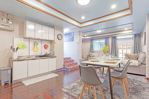 A modern kitchen with white cabinets, a dining area with a table and chairs, and a living area with a sofa and a window. - Large House in the Middle of Sukhumvit 22 for Family (Bangkok)