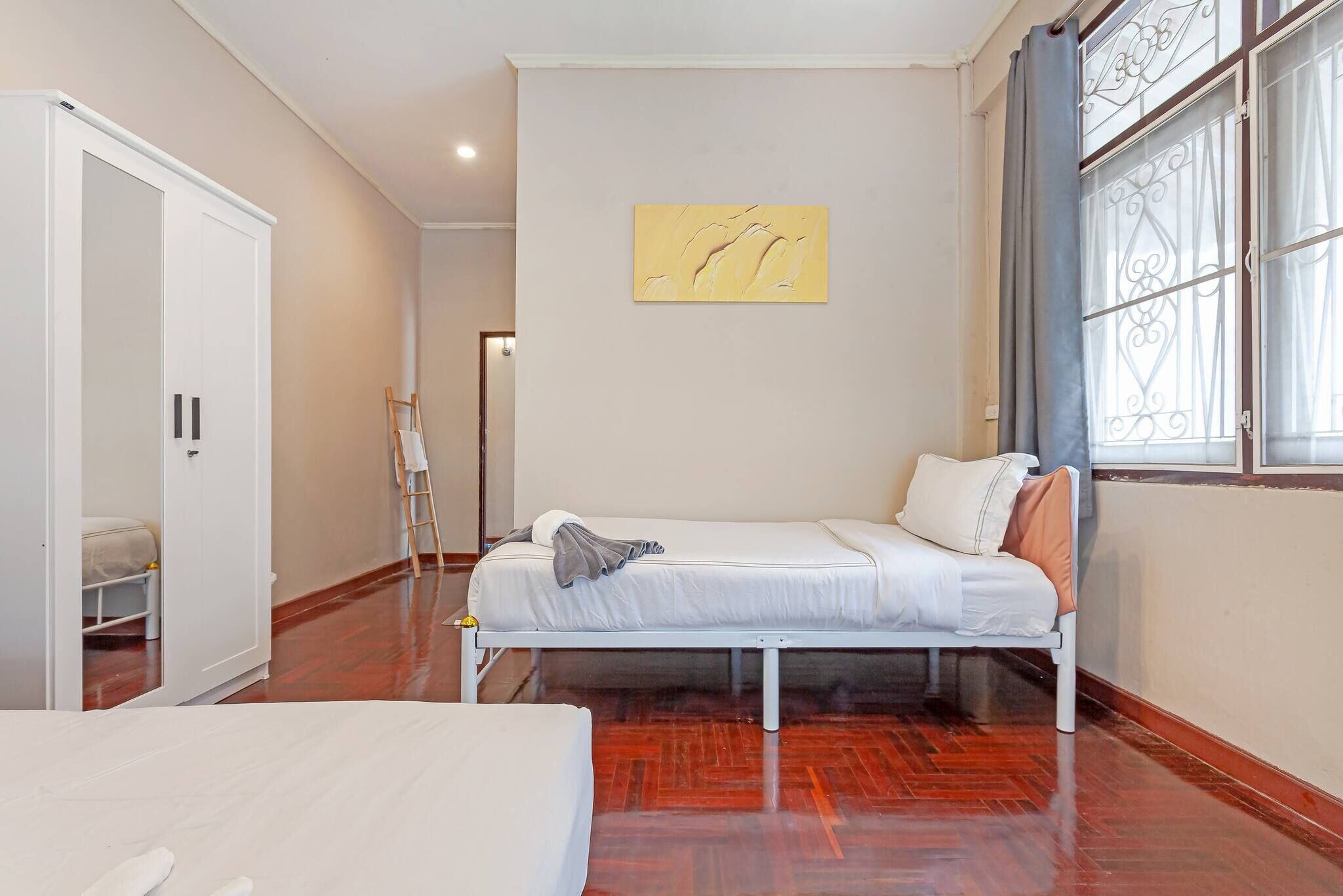 A bedroom with a bed, a wardrobe, a painting, and a window with curtains.