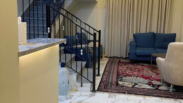 A modern living room with a staircase, blue sofa, and a patterned rug.
