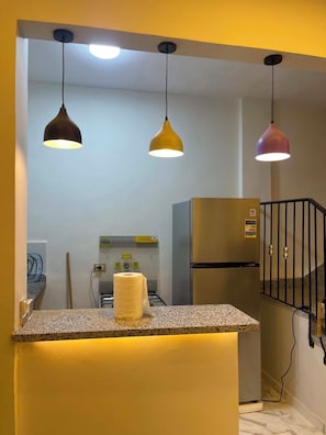 A kitchen with a central island, three pendant lights, a refrigerator, and a gas stove. - sheikh zayed mini villa (Sheikh zayed city)