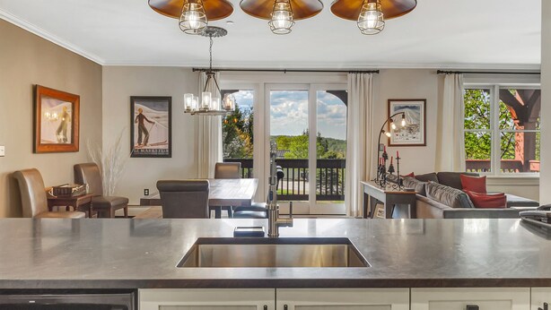 A modern kitchen with a large island, pendant lights, and a dining area with a view. - Luxury Stratton Village Condo | Walk to Lifts, Dining & Amenities (Stratton,)