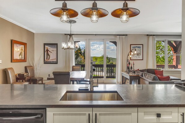 A modern kitchen with a large island, pendant lights, and a dining area with a view. - Luxury Stratton Village Condo | Walk to Lifts, Dining & Amenities (Stratton,)