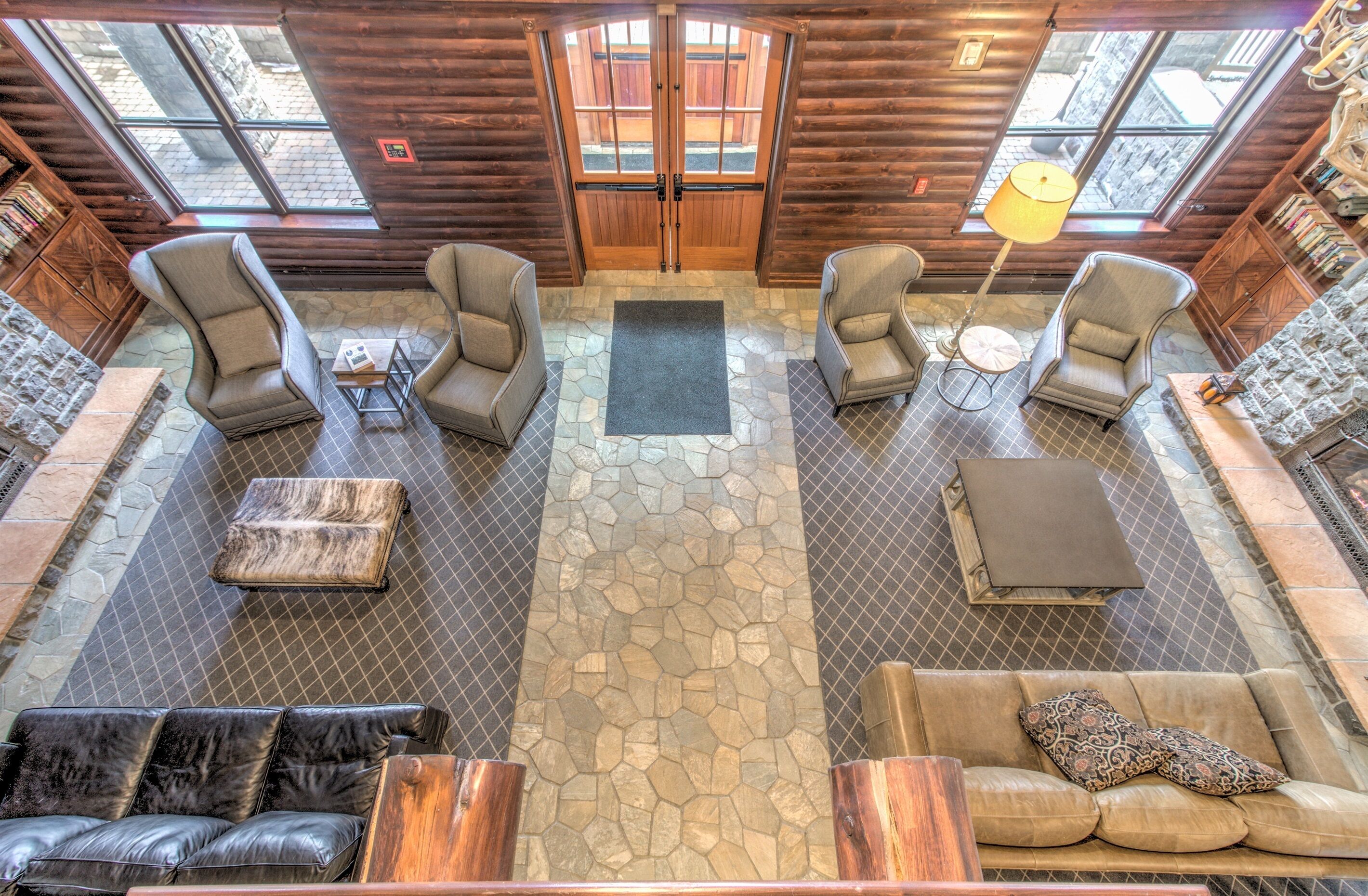A log cabin interior with a stone floor, leather seating, and a large wooden door.