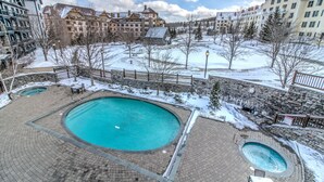 A resort with a large central pool, stone pathways, and snow-covered surroundings. - Luxury Stratton Village Condo | Walk to Lifts, Dining & Amenities (Stratton,)