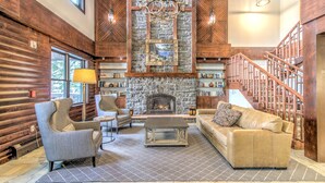 A log cabin interior with a stone fireplace, wooden staircase, and cozy seating area. - Luxury Stratton Village Condo | Walk to Lifts, Dining & Amenities (Stratton,)