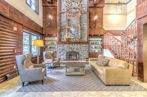 A log cabin interior with a stone fireplace, wooden staircase, and cozy seating area. - Luxury Stratton Village Condo | Walk to Lifts, Dining & Amenities (Stratton,)