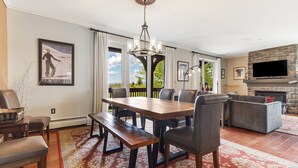 A dining area with a wooden table and benches, a chandelier, and a fireplace. - Luxury Stratton Village Condo | Walk to Lifts, Dining & Amenities (Stratton,)