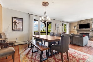 A dining area with a wooden table and benches, a chandelier, and a fireplace. - Luxury Stratton Village Condo | Walk to Lifts, Dining & Amenities (Stratton,)