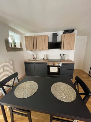 Une cuisine moderne avec des meubles de rangement noirs, un four encastré et un four à micro-ondes. On y trouve une table à manger avec deux sets de table et des chaises noires.