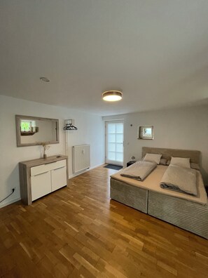 Een slaapkamer met een bed, een dressoir, een radiator en een raam met zonwering.