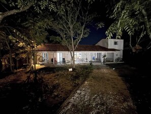 Una casa con techo de tejas, un porche cubierto y un jardín por la noche.