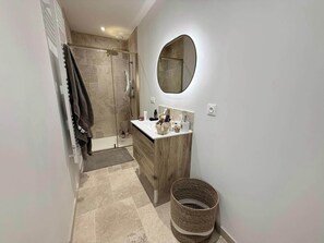 Un baño con ducha, lavabo, espejo y perchero para toallas.