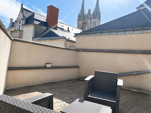 Une terrasse sur le toit, aménagée avec du mobilier d’extérieur, un pot de fleurs et offrant une vue sur une cathédrale.