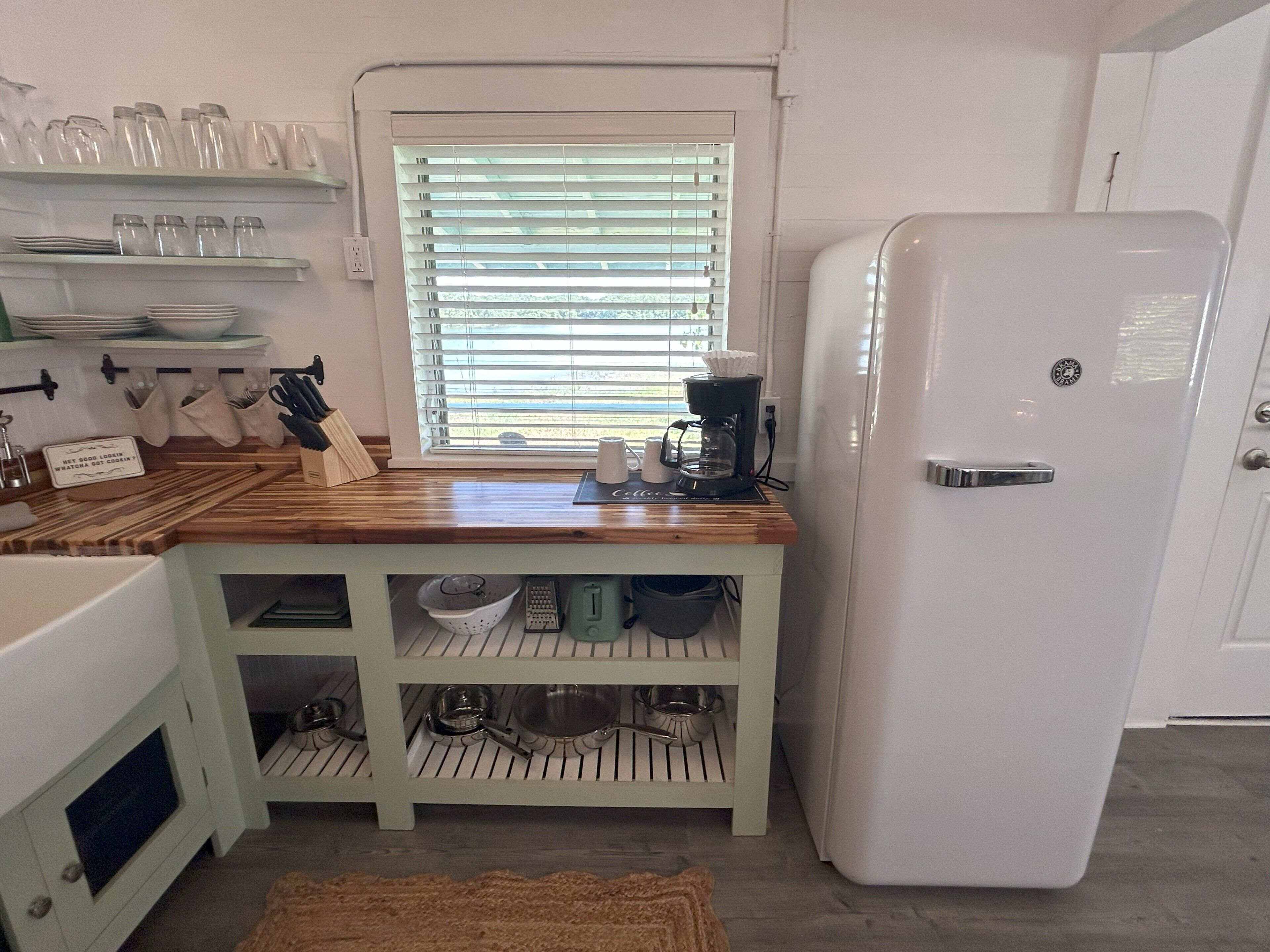 A kitchen with a white refrigerator, wooden countertop, and a window with blinds.